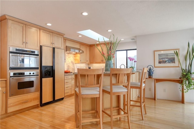 kitchen featuring paneled built in fridge, a skylight, light brown cabinetry, stainless steel double oven, and ventilation hood