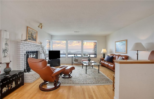 living room featuring visible vents, a brick fireplace, and wood finished floors