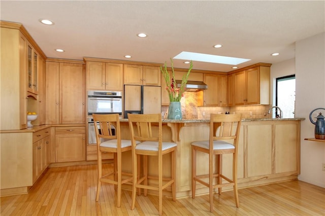 kitchen with stainless steel oven, light wood-style floors, paneled built in refrigerator, and a skylight