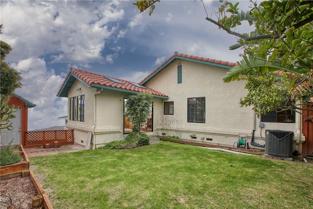 back of house featuring central air condition unit, a tiled roof, a vegetable garden, a yard, and stucco siding