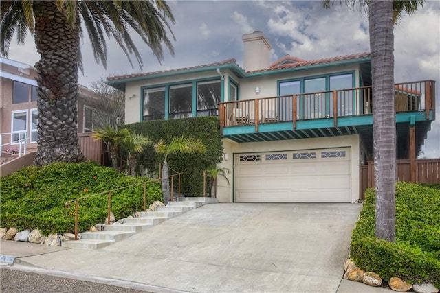 view of front of property featuring a balcony, a chimney, concrete driveway, a garage, and stucco siding