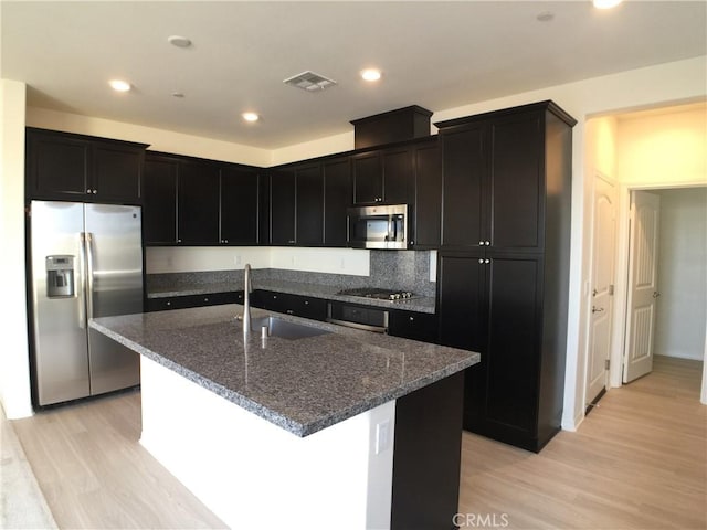 kitchen featuring visible vents, stainless steel appliances, dark stone countertops, a sink, and light wood-type flooring