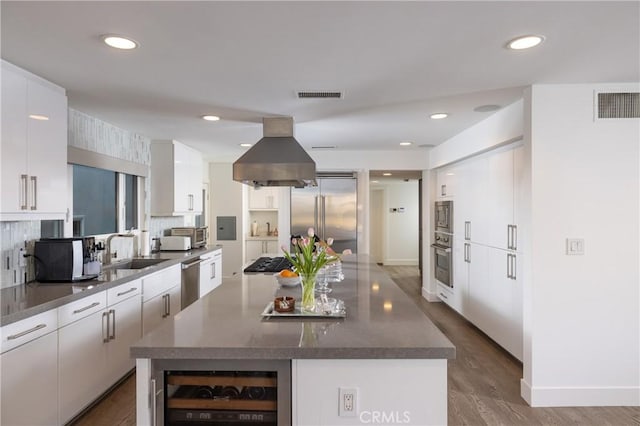 kitchen featuring visible vents, island exhaust hood, wine cooler, a sink, and built in appliances