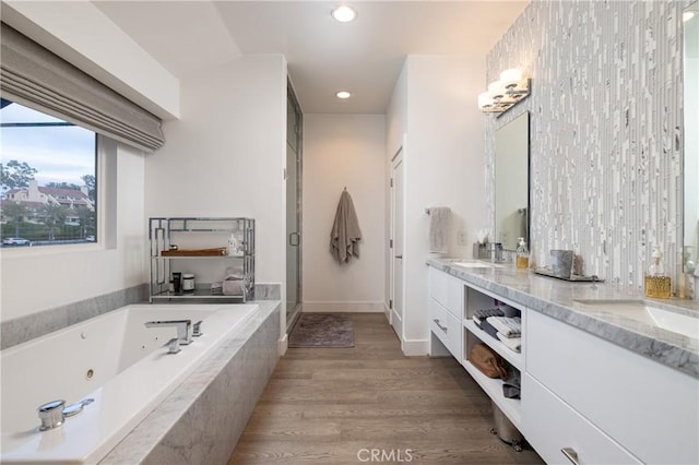 full bathroom featuring a shower stall, double vanity, wood finished floors, a sink, and a whirlpool tub
