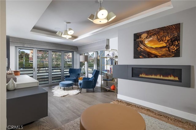 living area with baseboards, wood finished floors, a glass covered fireplace, and a raised ceiling