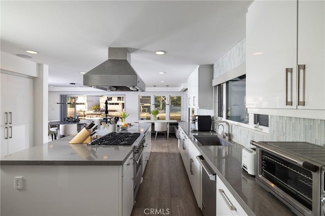 kitchen featuring white cabinetry, a kitchen island, a sink, wall chimney range hood, and appliances with stainless steel finishes