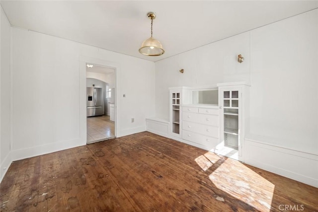 empty room with arched walkways, baseboards, and hardwood / wood-style floors