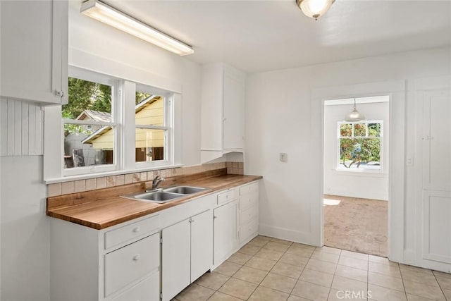 kitchen featuring white cabinets, light tile patterned floors, light carpet, and a sink