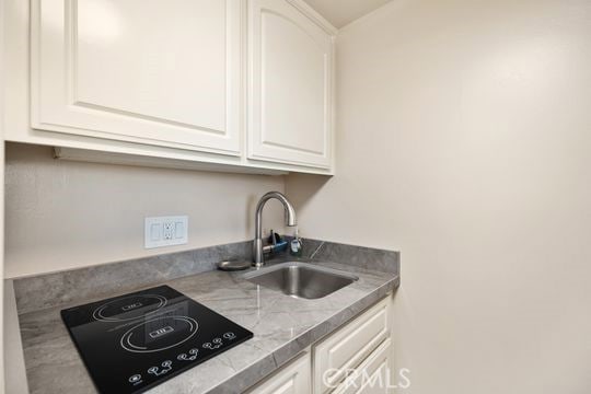 kitchen featuring black electric cooktop, white cabinets, and a sink