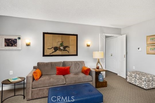 living area featuring carpet flooring, baseboards, and a textured ceiling