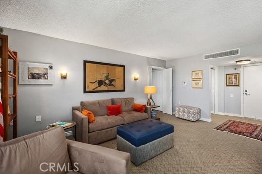 carpeted living room with baseboards, a textured ceiling, and visible vents