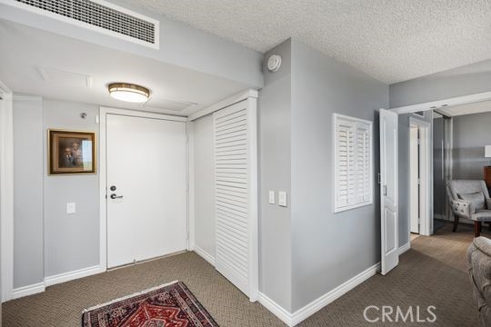 carpeted foyer featuring baseboards, a textured ceiling, and visible vents