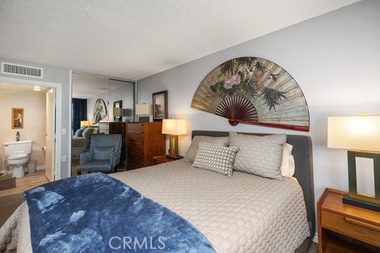 bedroom with visible vents, wood finished floors, ensuite bathroom, and a textured ceiling