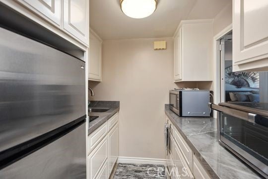 kitchen featuring white cabinets, a sink, appliances with stainless steel finishes, and baseboards