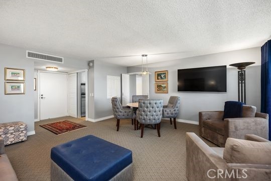 carpeted living room with baseboards, a textured ceiling, and visible vents