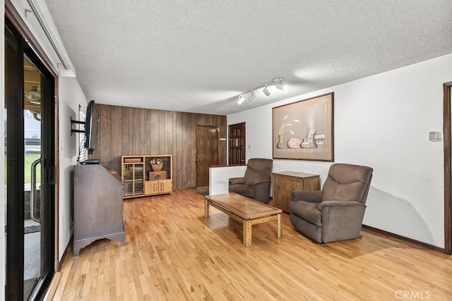 sitting room featuring wooden walls, baseboards, light wood-style floors, and a textured ceiling