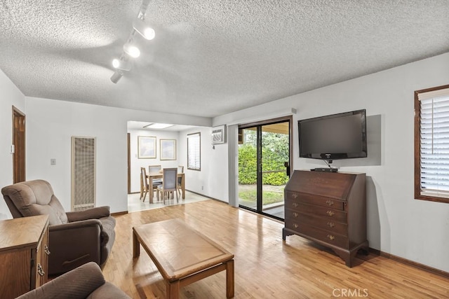 living area featuring baseboards, light wood-style flooring, and a textured ceiling