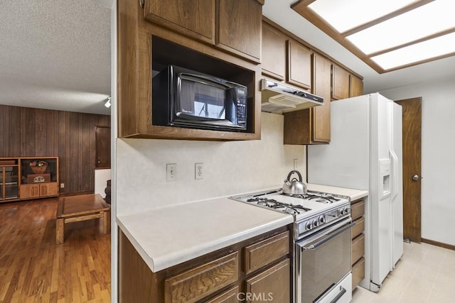 kitchen featuring a textured ceiling, light countertops, white range with gas cooktop, under cabinet range hood, and black microwave