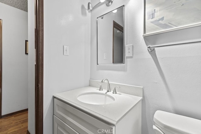 half bath featuring a textured ceiling, toilet, vanity, and wood finished floors