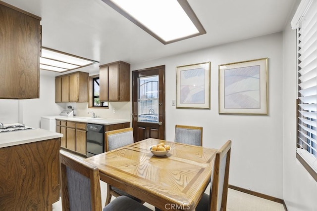 kitchen with light countertops, baseboards, washer / clothes dryer, a sink, and black dishwasher