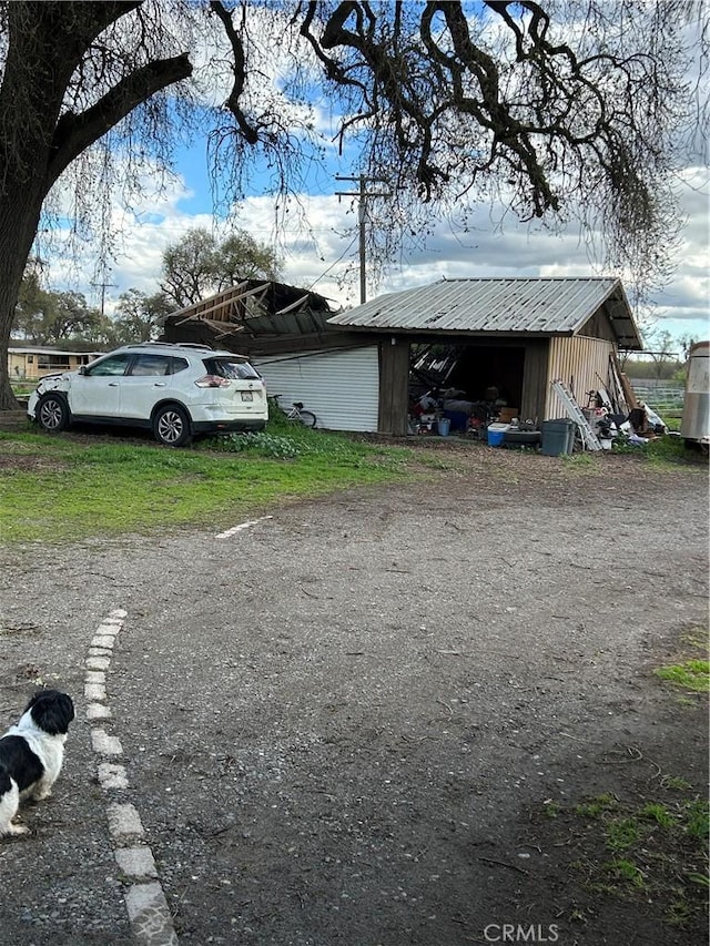 view of side of home with an outdoor structure, metal roof, and dirt driveway