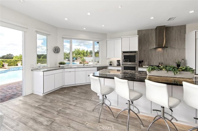 kitchen featuring wall chimney range hood, appliances with stainless steel finishes, a breakfast bar, a sink, and modern cabinets