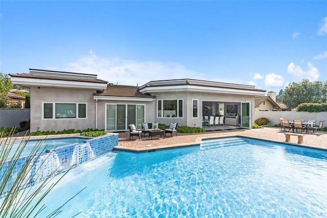 rear view of house with stucco siding, a pool with connected hot tub, fence, a patio area, and outdoor dining space