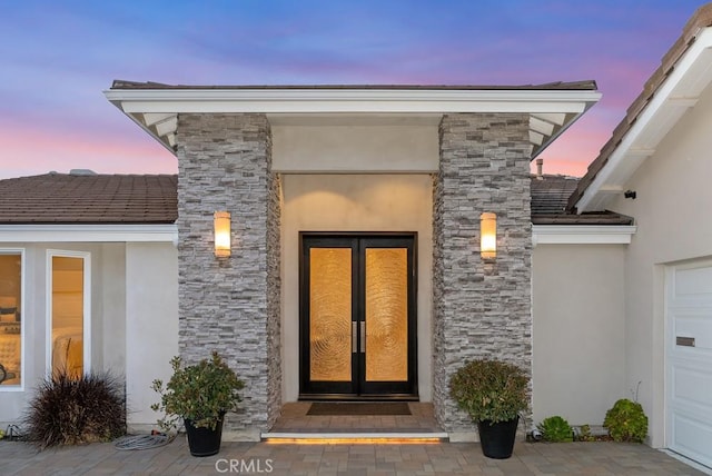 exterior entry at dusk featuring stucco siding, stone siding, and an attached garage