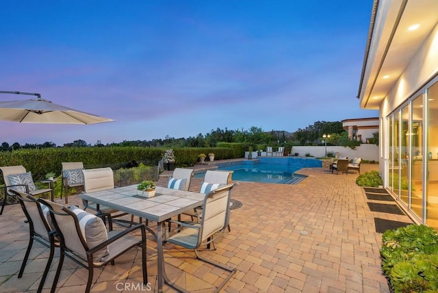 pool at dusk featuring outdoor dining area and a patio