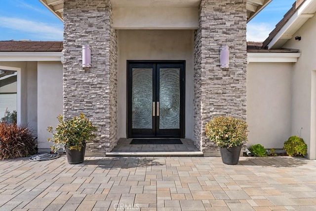 property entrance with french doors, stucco siding, and stone siding