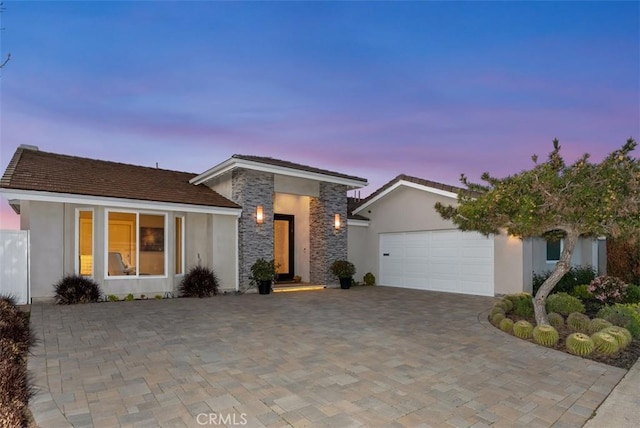 view of front of home with stucco siding, a garage, stone siding, and driveway