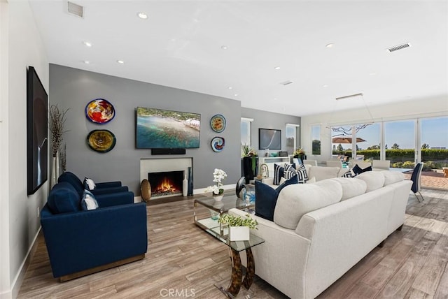 living room featuring light wood finished floors, baseboards, recessed lighting, and a lit fireplace
