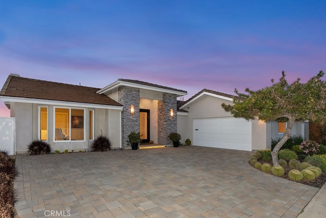 view of front of house featuring stucco siding, a garage, stone siding, and driveway