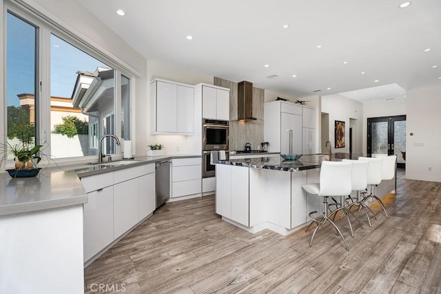 kitchen featuring a sink, stainless steel appliances, wall chimney range hood, modern cabinets, and recessed lighting