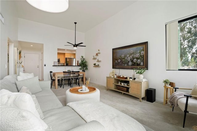 living area with ceiling fan, baseboards, high vaulted ceiling, and light colored carpet
