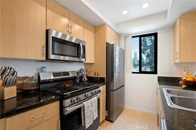 kitchen with dark stone countertops, light tile patterned flooring, baseboards, light brown cabinets, and appliances with stainless steel finishes