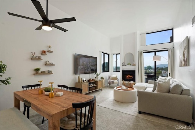 living room with high vaulted ceiling, ceiling fan, carpet floors, and a lit fireplace