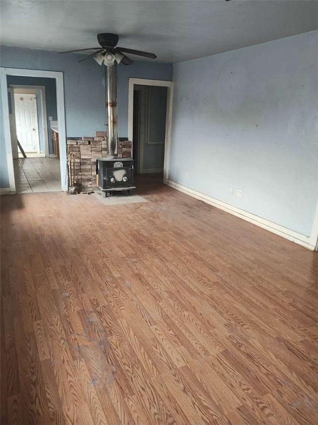 107 N Rine St, Alturas, CA 96101 - unfurnished living room featuring a wood stove, wood finished floors, ceiling fan, and baseboards