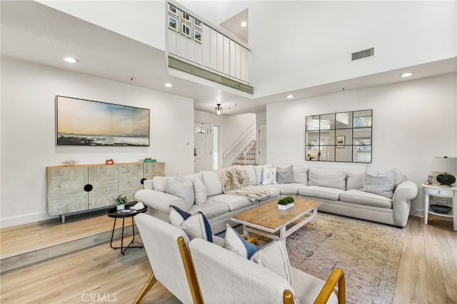 living room featuring light wood-style flooring, a towering ceiling, stairway, and visible vents