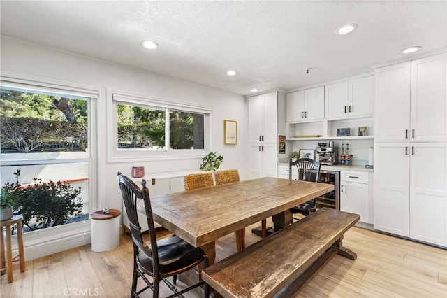dining room featuring light wood-style floors, a dry bar, recessed lighting, and a textured ceiling