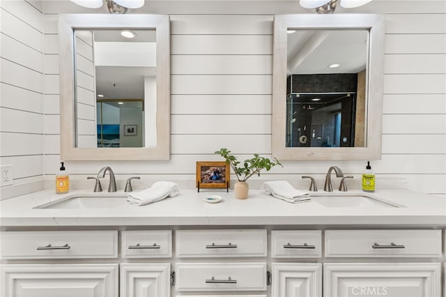 bathroom featuring double vanity, a shower with shower door, wood walls, and a sink