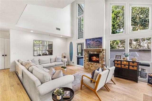 living area featuring a fireplace, a high ceiling, light wood-style flooring, and visible vents