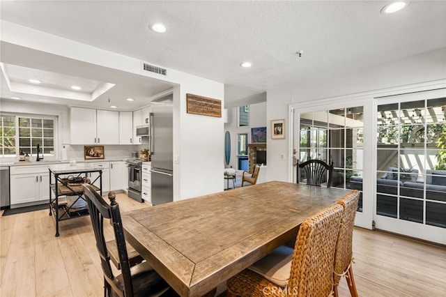 dining space with light wood-style flooring, plenty of natural light, and visible vents