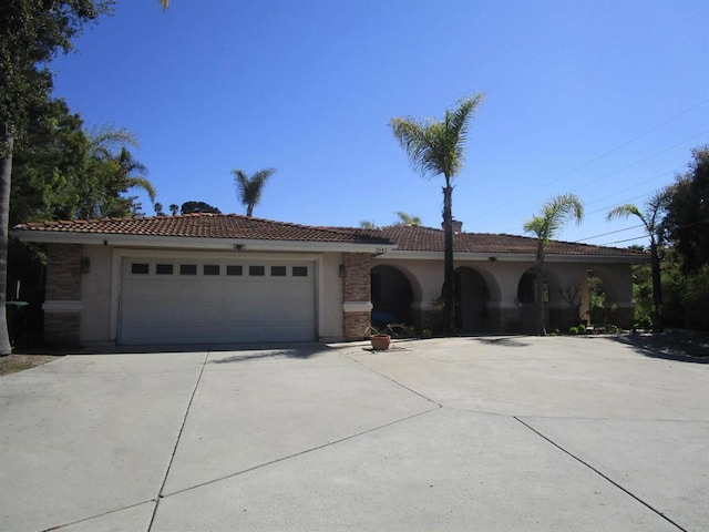 mediterranean / spanish house with driveway, a tile roof, stone siding, stucco siding, and a garage