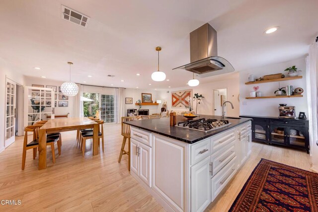 1009 Grandview Ave, Ojai, CA 93023 - kitchen featuring island range hood, stainless steel gas cooktop, white cabinetry, light wood-type flooring, and a kitchen island with sink