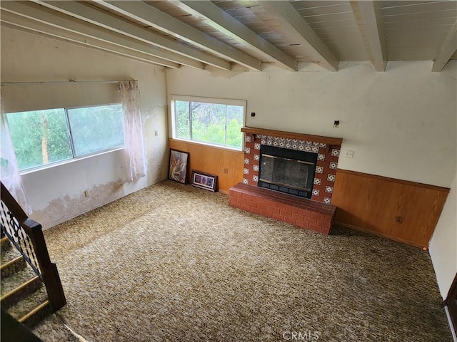 unfurnished living room with wooden walls, beam ceiling, and carpet floors