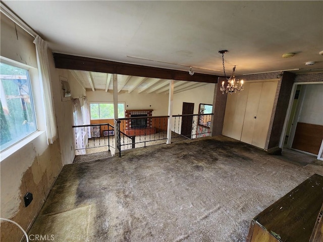 unfurnished living room featuring beam ceiling, an inviting chandelier, and carpet floors