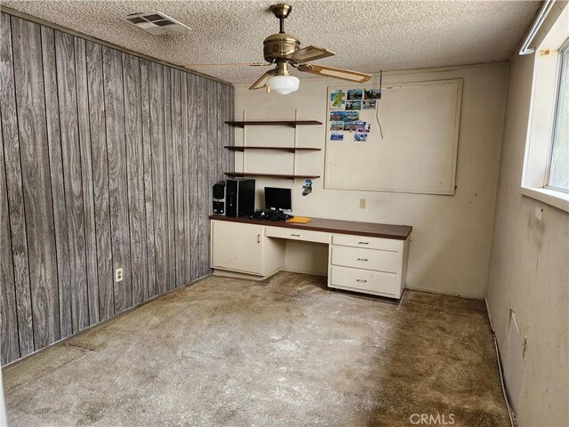 unfurnished office with wood walls, ceiling fan, built in study area, and visible vents