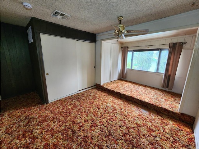 unfurnished bedroom with carpet, a textured ceiling, a ceiling fan, visible vents, and wood walls