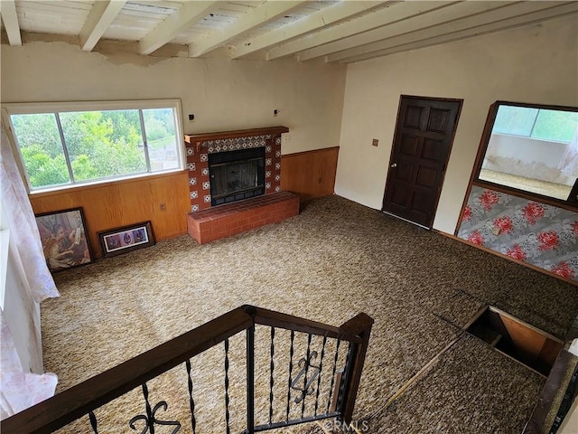 carpeted living room featuring a tile fireplace, a wainscoted wall, beamed ceiling, and wooden walls